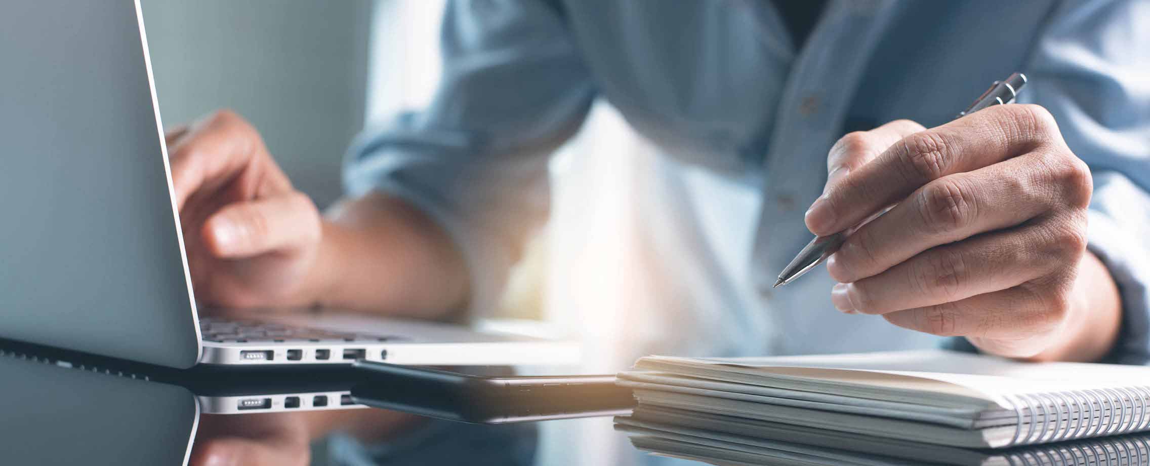 Photo d'une personne travaillant sur son portable et écrivant dans un carnet